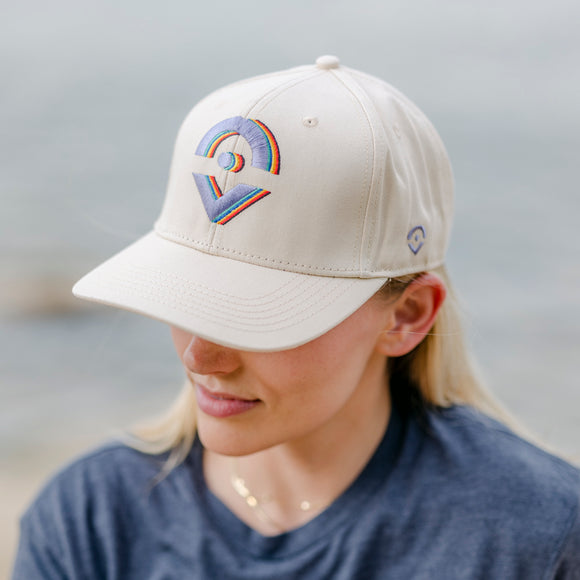 Cream colored hat with rainbow embroidered Outsider logos on the front modeled on woman